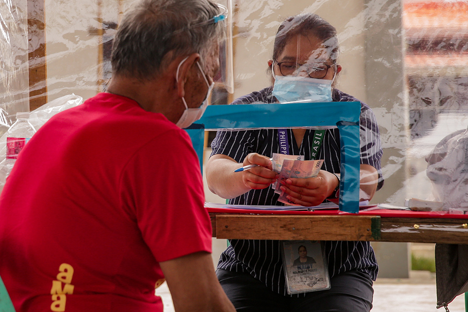 A government worker hands out financial aid at a covered court in Barangay Tibaguin, Hagonoy, Bulacan on April 20, 2021. George Calvelo, ABS-CBN News/File