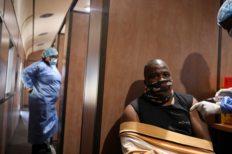 Dennis Malattji takes his coronavirus disease (COVID-19) vaccine while a health worker looks on inside the Transvaco COVID-19 vaccine train, as South Africa