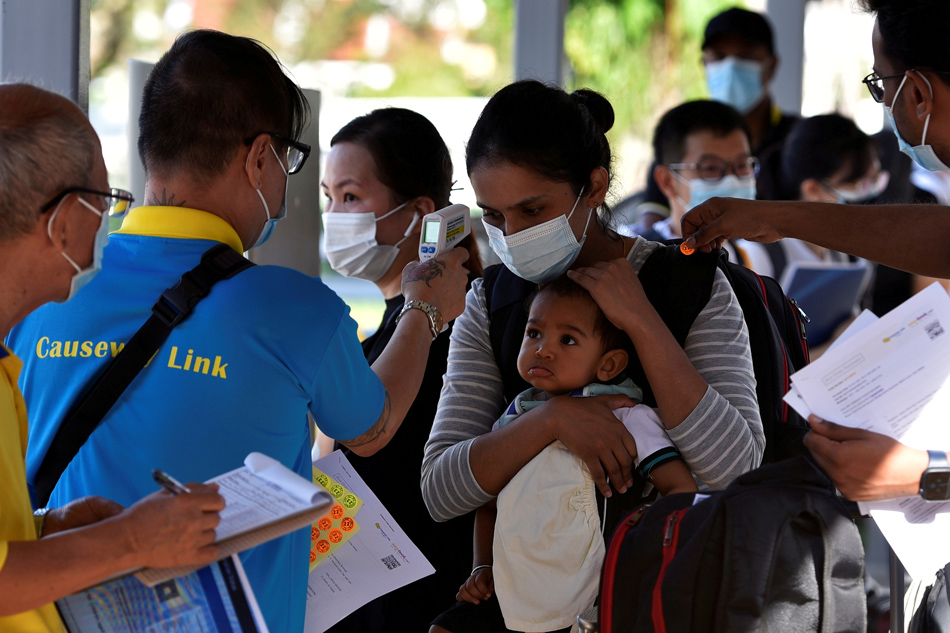  A mother and child get their temperatures checked as they prepare to board a bus back to Malaysia at a station in Singapore, November 29, 2021. Caroline Chia, Reuters