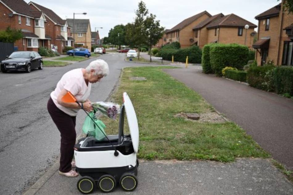 A 71-year-old woman picks up a delivery from an autonomous robot called Starship delivering groceries from a nearby Co-op supermarket in Milton Keynes, England on September 20, 2021. Daniel Leal-Olivas, AFP