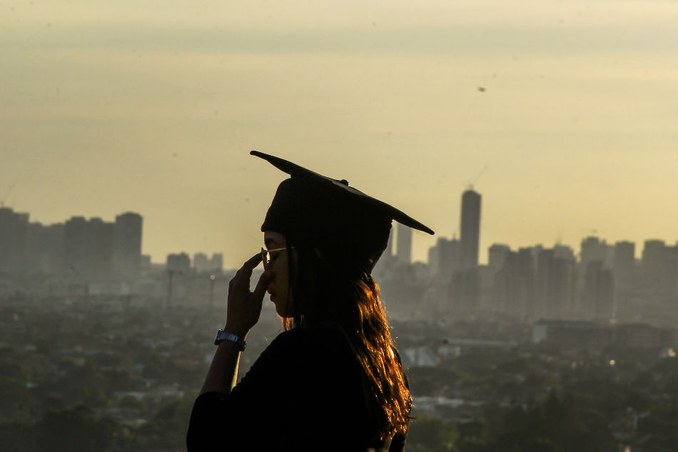 A young woman in her graduation cap poses for her boyfriend as he takes pictures of her with the cityscape in the background as seen from Antipolo City, March 19, 2019. Jonathan Cellona, ABS-CBN News