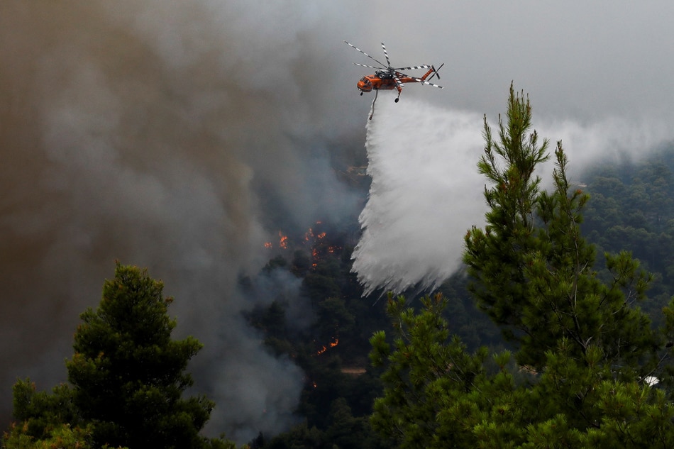 A firefighting helicopter makes a water drop as wildfire burns at the village of Ippokratios Politia, north of Athens, Greece on August 6, 2021. 