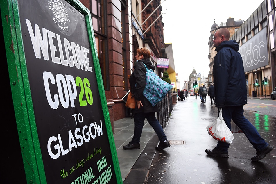 People walk into a pub past a COP26 sign in the city center of Glasgow, Scotland on October 29, 2021, ahead of the COP26 UN Climate Change Conference to be held in the city from October 31, 2021. Britain's Prime Minister Boris Johnson will host more than 120 leaders in Glasgow, before the UN meeting spends a fortnight tackling the work of deciding how to limit temperature rises to 1.5 degrees Celsius. Andy Buchanan, AFP 