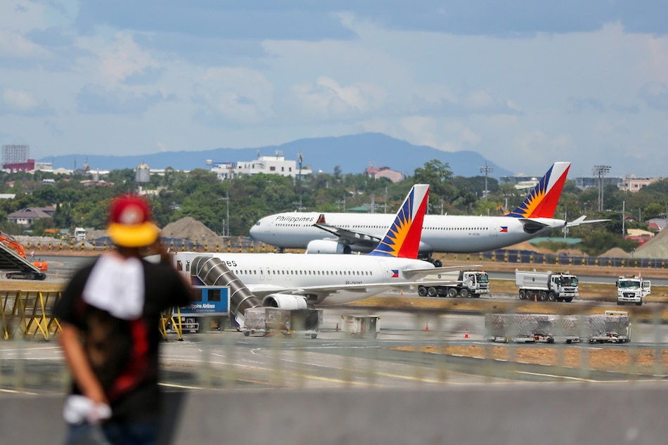 A Philippine Airlines plane is seen at the background as a man uses his phone at the arrival area of the Ninoy Aquino International Airport (NAIA) Terminal 1 in Pasay City on May 24, 2021. Jonathan Cellona, ABS-CBN News