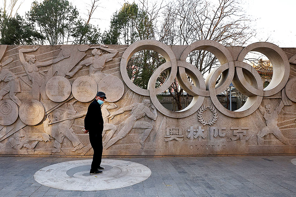 man stands in front of a base relief containing the Olympic Rings rtr