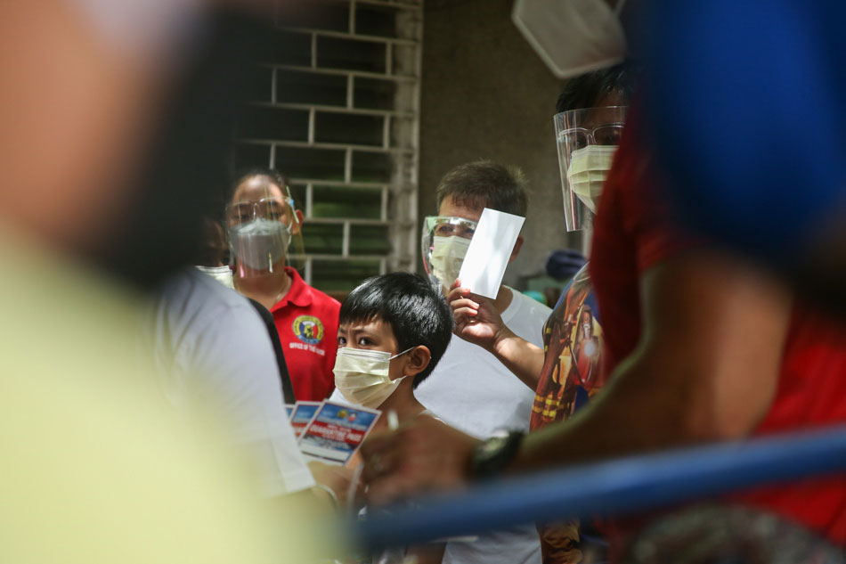 Residents wait as authorities distribute quarantine passes in Barangay Batis, San Juan