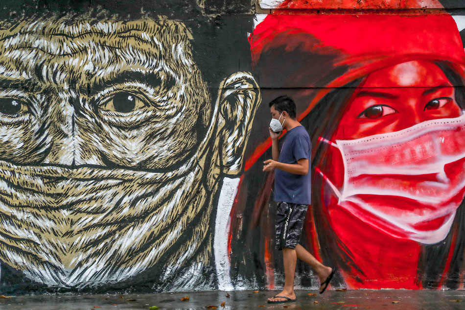 People pass by a mural by artists Sim Tolentino, Bryan Barrios and Moks featuring images of people during the COVID-19 pandemic painted on the walls of the Columban Missionaries building on Singalong Street in Manila, September 06, 2021. Jonathan Cellona, ABS-CBN News