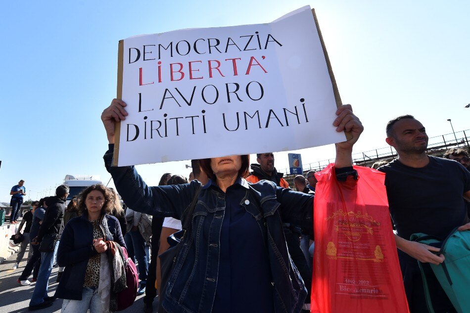 A person holds a banner as port workers gather outside the entrance to protest against the implementation of the COVID-19 health pass, the Green Pass, in the workplace, in Genoa, Italy, on October 15, 2021. The banner reads 'Democracy, freedom, work, human rights'. Massimo Pinca, Reuters