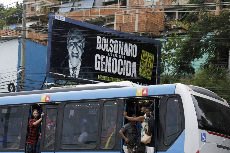 Passengers travel on a crowded public bus past a banner against Brazil's President Jair Bolsonaro and his policies on the COVID-19 pandemic, in Rio de Janeiro on April 6, 2021. The banner reads 