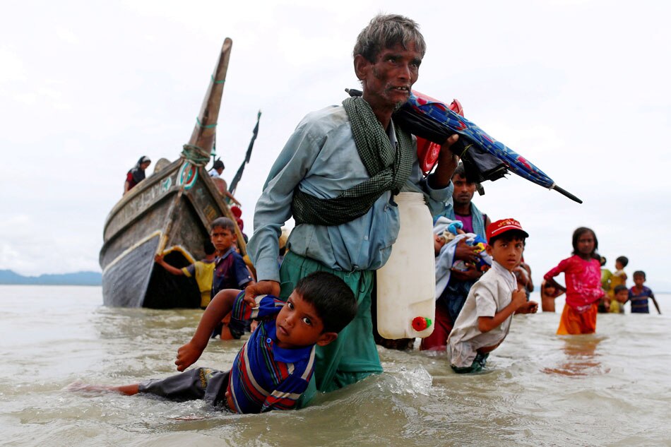 A Rohingya refugee pulls a child as they walk to the shore after crossing the Bangladesh-Myanmar border by boat through the Bay of Bengal in Shah Porir Dwip, Bangladesh, Sept. 10, 2017. 