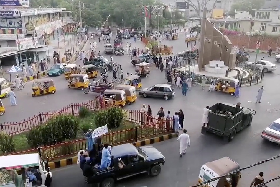 Taliban militants waving a Taliban flag on the back of a pickup truck drive past a crowded street at Pashtunistan Square area in Jalalabad, Afghanistan in this still image taken from social media video uploaded on August 15, 2021. Social media website/via Reuters