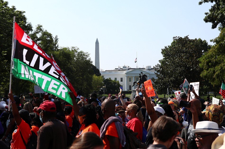 Demonstrators, of which one carries a Black Lives Matter flag, walk past the White House at an anti voter suppression laws march Washington, U.S., August 28, 2021. Tom Brenner, Reuters