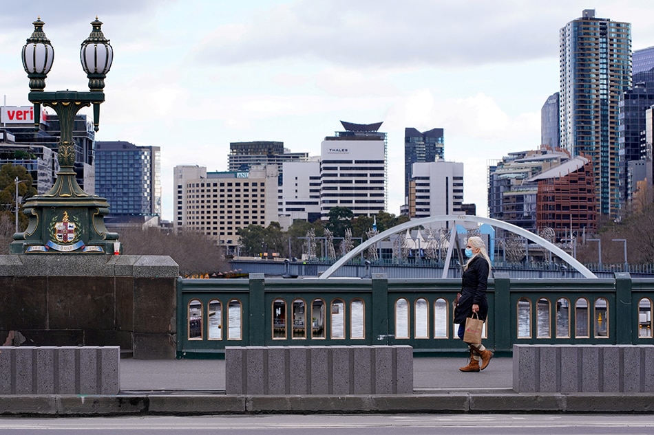 A lone woman, wearing a protective face mask, walks across a city centre bridge as the state of Victoria looks to curb the spread of a COVID-19 outbreak in Melbourne, Australia, July 16, 2021. Sandra Sanders, Reuters/File