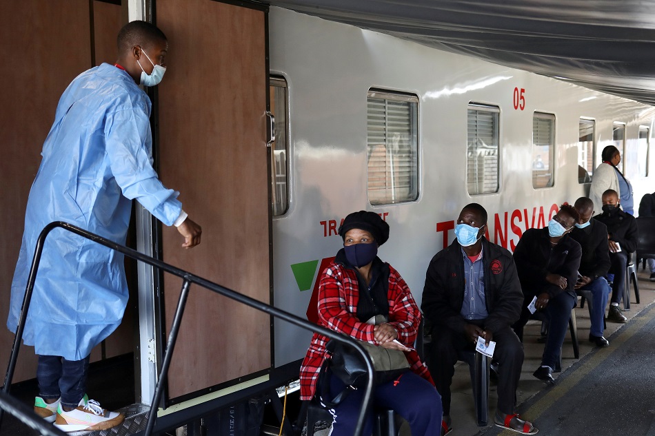 In this photo taken August 30, 2021, a health worker talks to people at the Springs train station on the East Rand, South Africa, as they wait to register next to the Transvaco COVID-19 vaccine train, after South Africa's rail company Transnet turned the train into a COVID vaccination center on rails to help the government speed up its vaccine rollout in the country's remote communities. Siphiwe Sibeko, Reuters/File