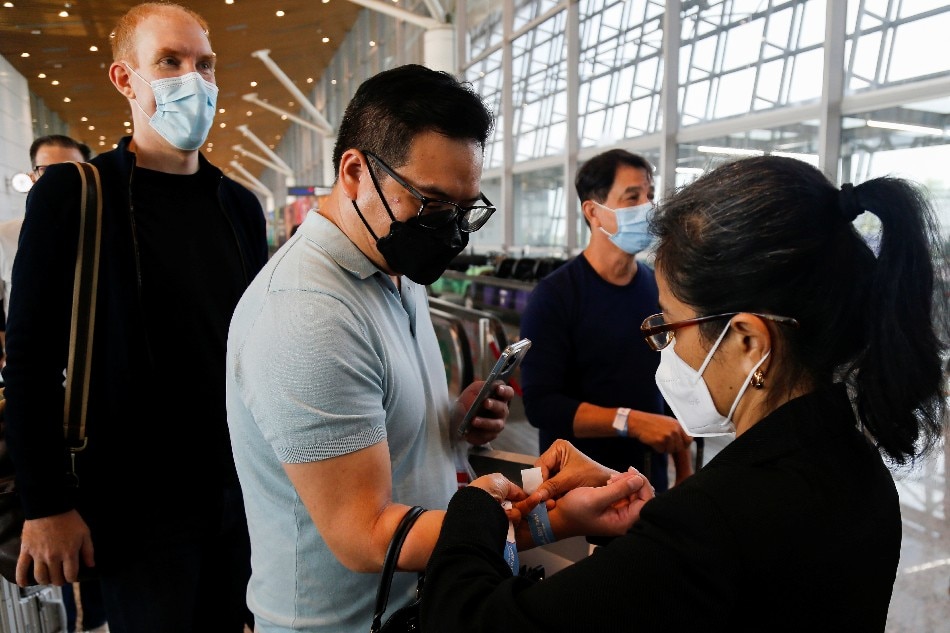 An airport staff puts a wristband on a traveller upon his arrival at the Kuala Lumpur International Airport under the Malaysia-Singapore Vaccinated Travel Lane program, in Sepang, Malaysia, Nov. 29, 2021. Lai Seng Sin, Reuters