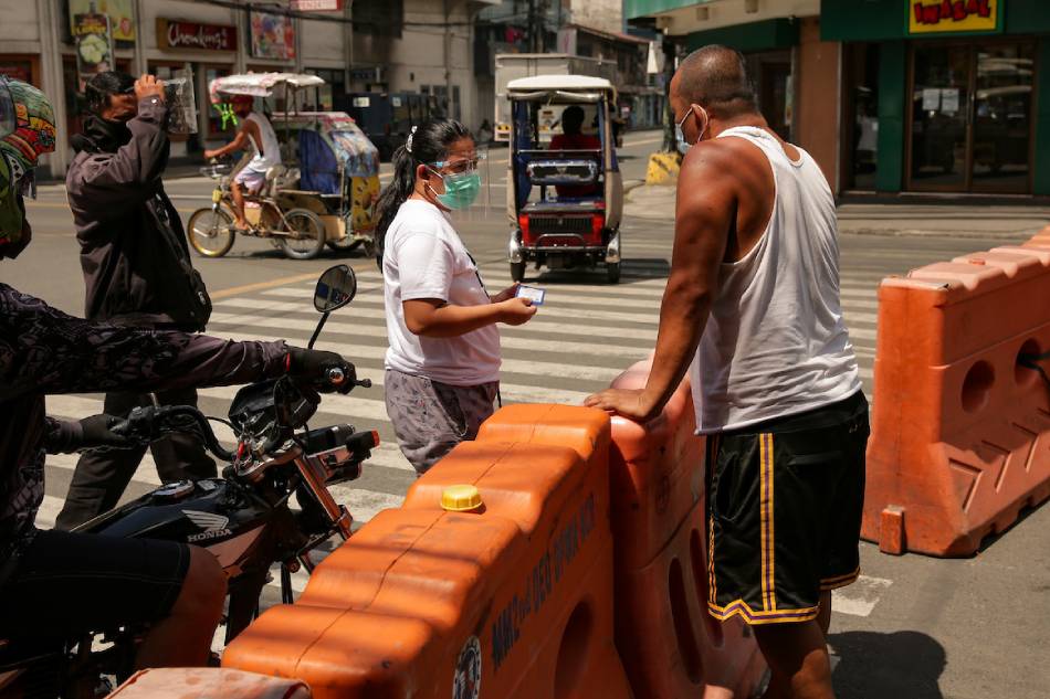 A barangay official inspects quarantine passes of people entering their jurisdiction at a street in Baclaran, Parañaque City on March 31, 2021. George Calvelo, ABS-CBN News