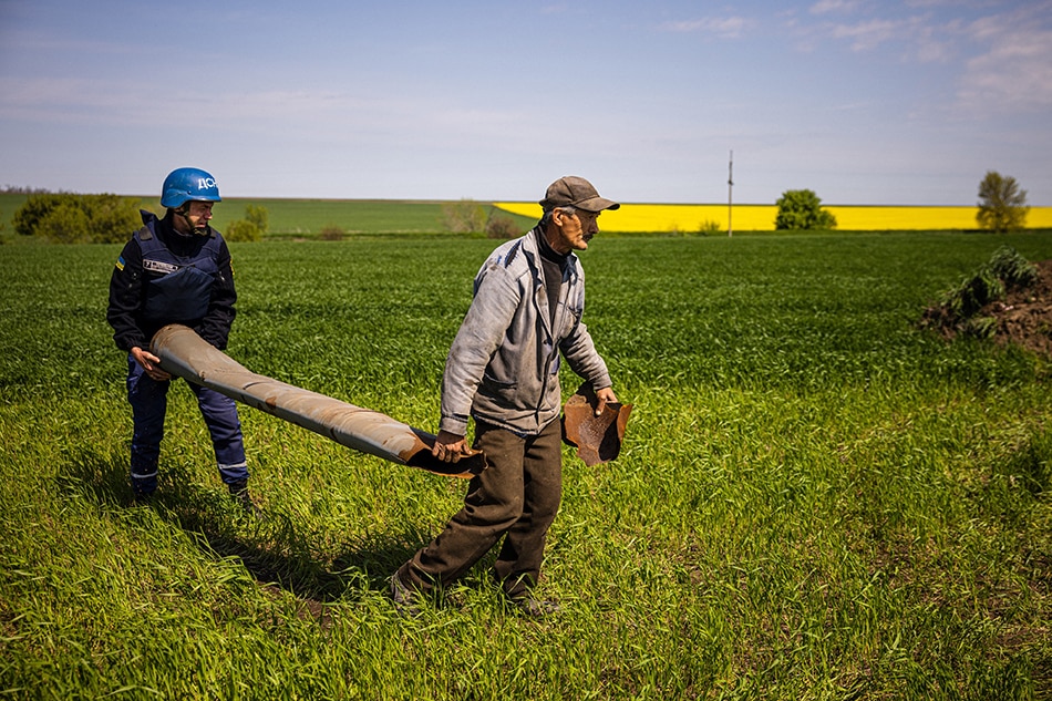 A farmer and a member of a demining team of the State Emergency Service of Ukraine carry an unexploded missile remaining near the village of Hryhorivka, Zaporizhzhia Region, on May 5, 2022, amid the Russian invasion of Ukraine. It's planting season in Ukraine and in addition to a spiking need for fuel and fertilizer, demining teams are flooded with calls to destroy the unexploded missiles or mines in fields, which in some places have wounded or killed farmers. Dimitar DILKOFF / AFP