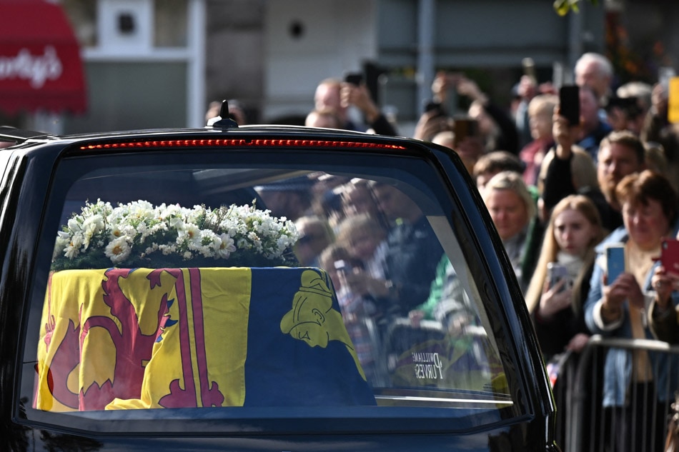 Members of the public pay their respects as the hearse carrying the coffin of Queen Elizabeth II, draped in the Royal Standard of Scotland, is driven through Ballater, on Sept. 11, 2022. Paul Ellis/AFP