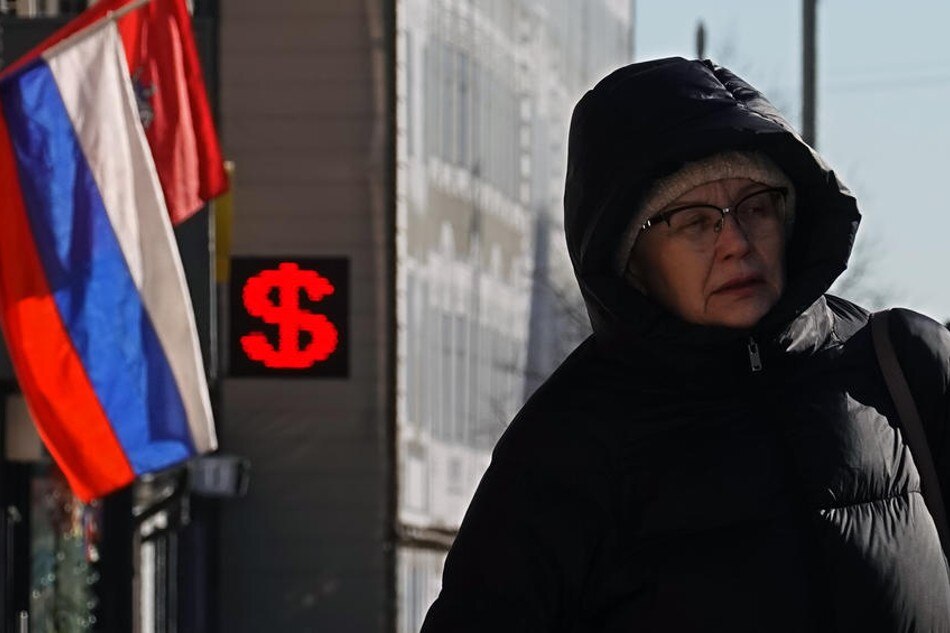 A woman walks in front of an electronic panel displaying the dollar sign at an exchange office in Moscow, Russia, March 10, 2022. Maxim Shipenkov, EPA-EFE/File
