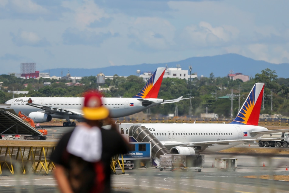 A Philippine Airlines plane is seen at the background as a man uses his phone at the arrival area of the Ninoy Aquino International Airport (NAIA) Terminal 1 in Pasay City on May 24, 2021. Jonathan Cellona, ABS-CBN News/File