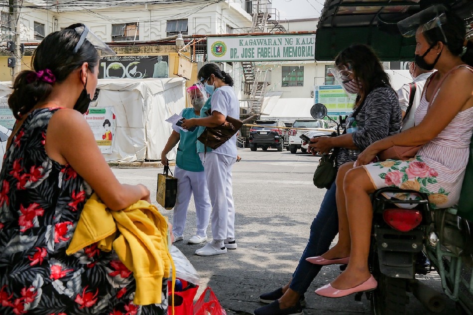 Health workers pass by as a pregnant woman and her companions as they wait for a ride home just outside the Dr. Jose Fabella Memorial Hospital in Manila on Aug. 19, 2021. George Calvelo, ABS-CBN News/File 