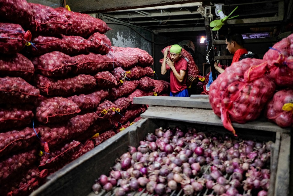 Workers unload bags of red onions inside a storage area in Divisoria market in Manila on Aug. 18, 2022. George Calvelo, ABS-CBN News/file