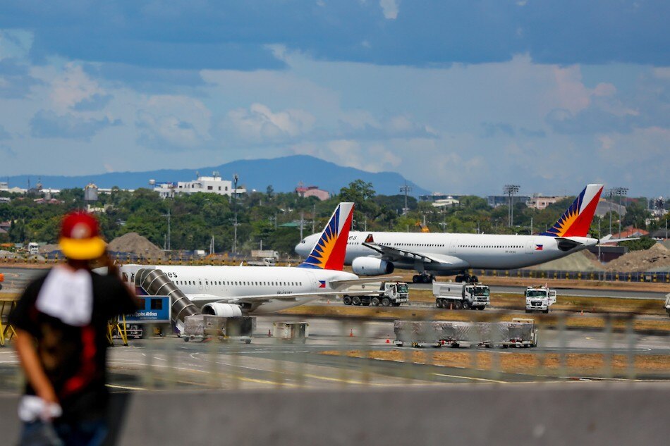 A Philippine Airlines plane is seen at the background as a man uses his phone at the arrival area of the Ninoy Aquino International Airport (NAIA) Terminal 1 in Pasay City on May 24, 2021. Jonathan Cellona, ABS-CBN News