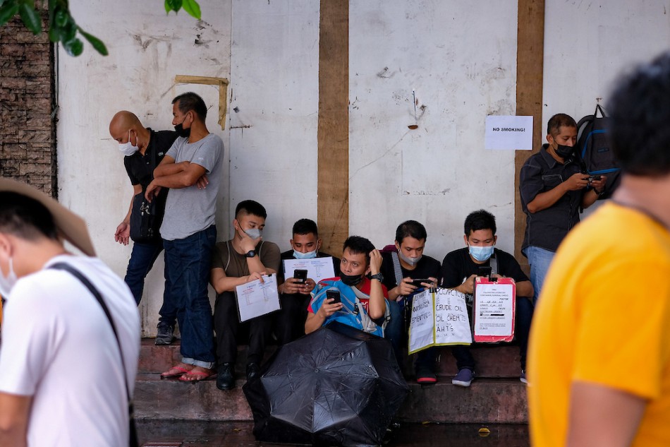 Job applicants take shelter from the rain as they line up outside the Luneta Seafarer’s Center in Manila on October 6, 2022. George Calvelo, ABS-CBN News
