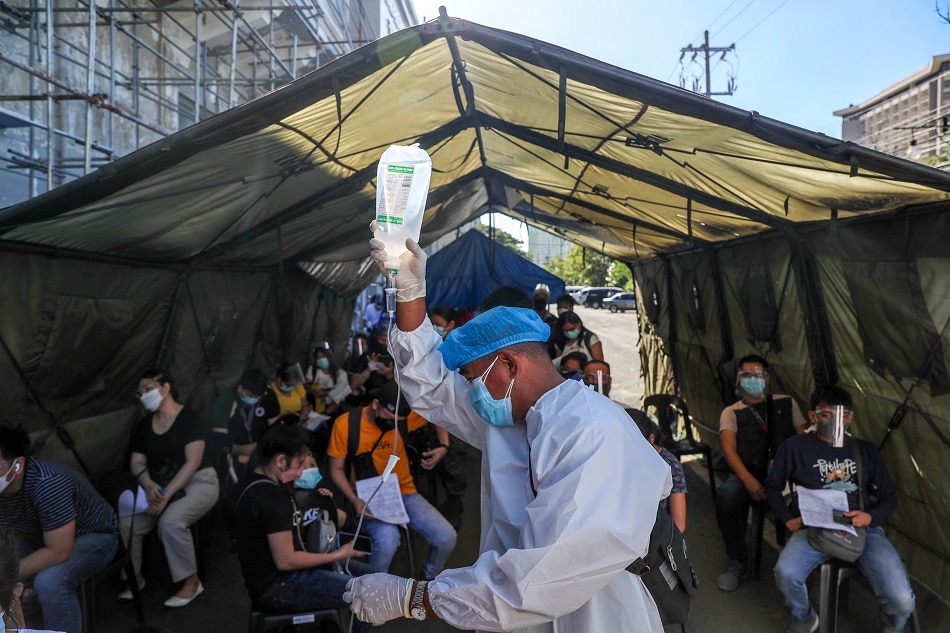 A health worker assists a hospital patient with her dextrose as she lines up with other people for swab test at a COVID-19 testing facility at the Rizal Memorial Coliseum in Manila on Jan. 4, 2022. The government raised the alert level to three in response to the sharp increase in the number of cases amid the threat of the Omicron variant. Jonathan Cellona, ABS-CBN News 