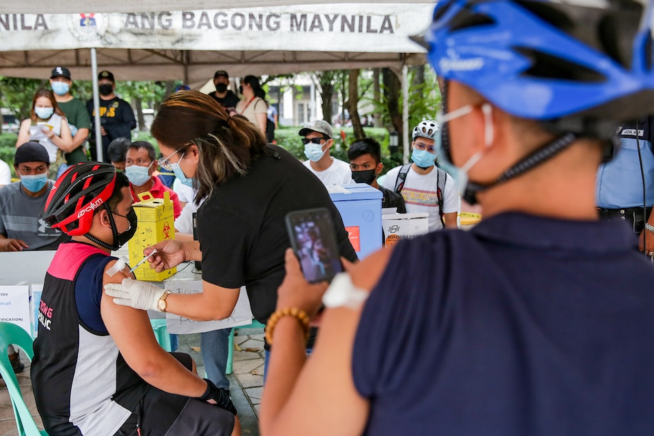 A man takes a picture of his fellow cyclist as he gets inoculated against COVID-19 at the Kartilya ng Katipunan beside the Manila City Hall on January 14, 2022. George Calvelo, ABS-CBN News