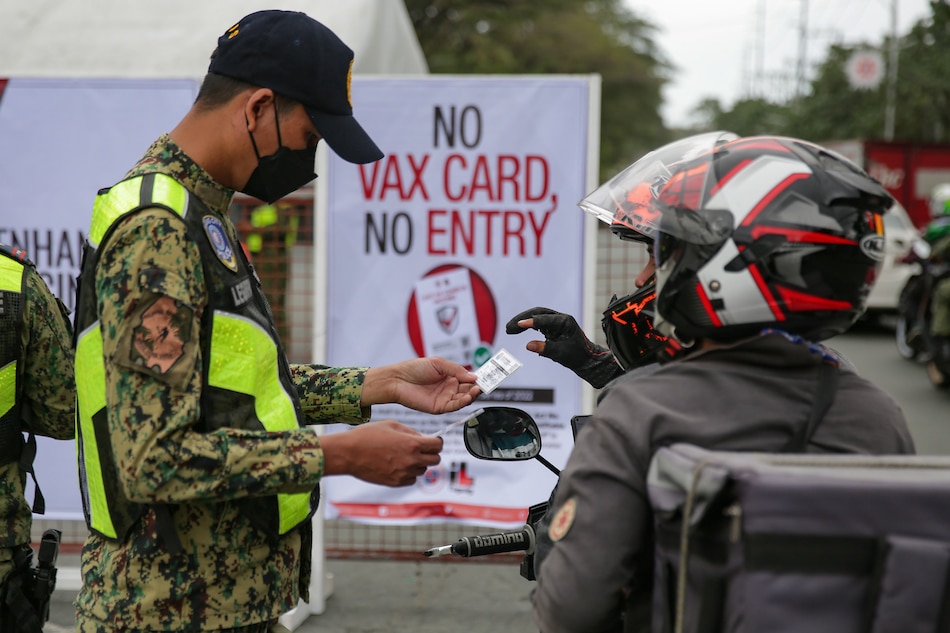 Police officers inspect vaccination cards of pedestrians and motorists passing through a busy road in Taguig City on January 21, 2022. George Calvelo, ABS-CBN News