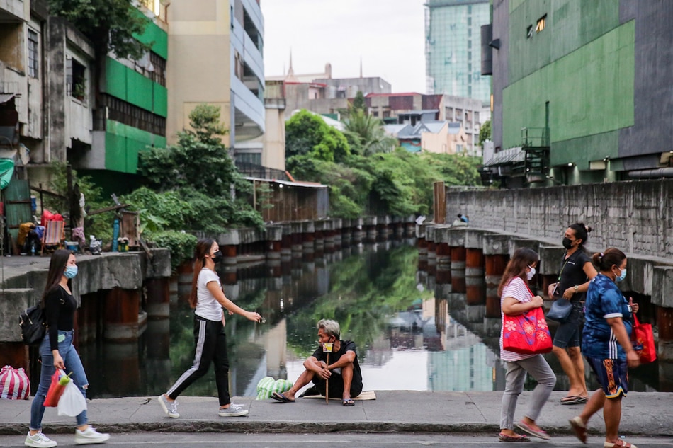 A homeless man sits beside a creek along Recto St. in Divisoria market in Manila on January 20, 2022 as pedestrians pass by. Preliminary results of the Asian Development Bank’s COVID-19 Country Assessment report shows the Philippines lagging its neighbors in a return to pre-pandemic growth rates with long-term effects of the pandemic on employment being a key concern. George Calvelo, ABS-CBN News