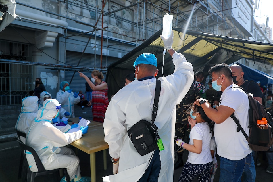 A health worker assists a hospital patient with her dextrose as she lines up with other people for swab test at a COVID-19 testing facility at the Rizal Memorial Coliseum in Manila on January 04, 2022. Jonathan Cellona, ABS-CBN News/File