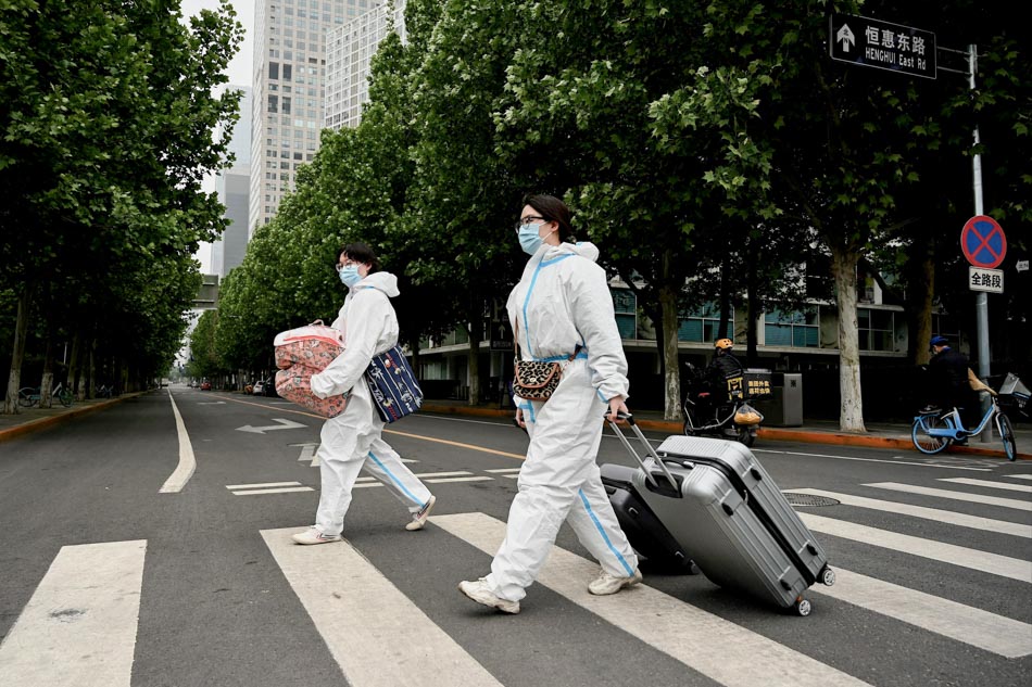 People wearing personal protective equipment (PPE) cross a street with their luggage near an area on lockdown due to the recent Covid-19 coronavirus outbreaks in Beijing on Tuesday. Millions of people in Beijing stayed home on May 9 as China's capital tries to fend off a Covid-19 outbreak with creeping restrictions on movement. Noel Celis, AFP