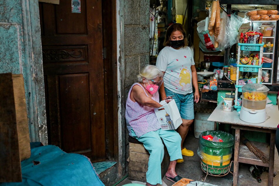 An elderly woman inspects the supplemental kit she received from the local government at a neighborhood in Tondo, Manila on August 12, 2021. The kit contains 400g of supplemental milk and a box of vitamins which are scheduled to be distributed to 150,000 senior citizens in the city. George Calvelo, ABS-CBN News]