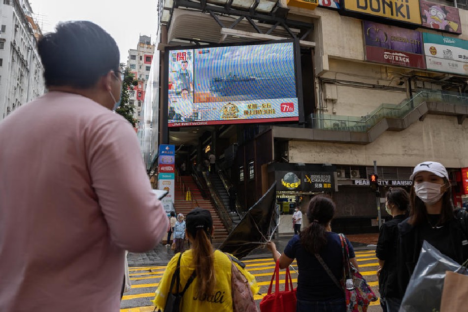 Pedestrians walk at a street past a large TV-screen displaying news broadcasting of a China