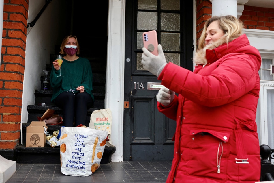 A woman self-isolating with COVID-19 sits on her doorstep as her mother, who delivered gifts and food, runs a video call with grandparents amid COVID-19 outbreak, in Putney, London on December 25, 2021. Kevin Coombs, Reuters