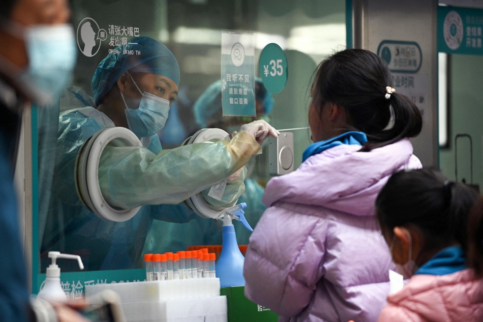 A health worker takes a swab sample from a girl to be tested for COVID-19 infection in Beijing on Monday, amid a record surge in infections across China. Noel Celis, AFP