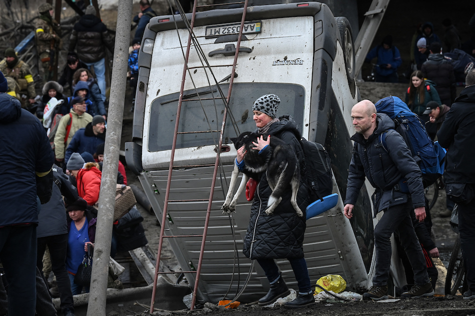 A woman carries a dog while people cross a destroyed bridge as they evacuate the city of Irpin, northwest of Kyiv, during heavy shelling and bombing on March 5, 2022, 10 days after Russia launched a military in vasion on Ukraine. Aris Messinis, AFP/File