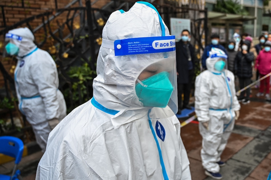 Workers wearing protective gear look on as people wait to be tested for COVID-19 at a residential compound in Shanghai on March 18, 2022. Hector Retamal, AFP/File