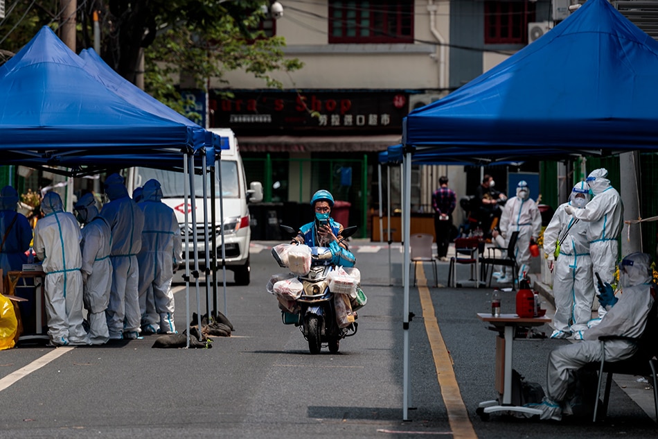 A delivery man rides a scooter through a road blockade and a makeshift COVID-19 testing site during the city lockdown in Shanghai, China, April 25, 2022. Alex Plavevski, EPA-EFE