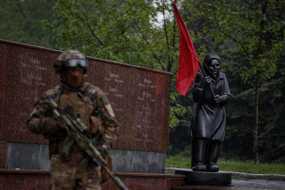 A picture taken during a visit to Mariupol organized by the Russian military shows a Russian serviceman standing next to a statue of a grandmother in Leninsky Komsomol Square in downtown of Mariupol, Ukraine, on May 18, 2022. Sergei Ilnitsky, EPA-EFE