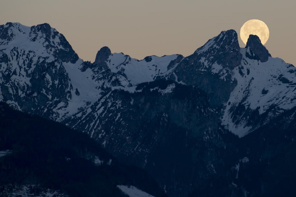 The full moon sets behind the mountains including the twin peaks of Les Jumelles in the Chablais Valaisan, seen from Fenalet-sur-Bex, Switzerland, January 18, 2022. Anthony Anex, EPA-EFE/file