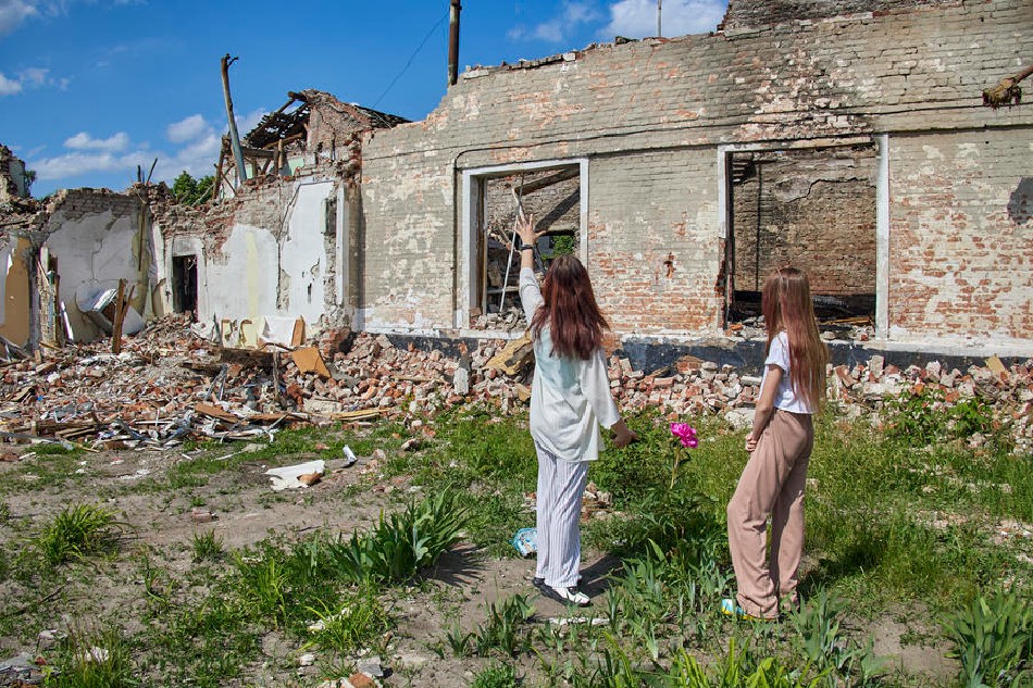 Children walk past a damaged school in the small city of Merefa in the Kharkiv area, Ukraine, June 1, 2022. Russian troops were recently pushed back by the Ukrainian army from the outskirts of the city. Kharkiv, Ukraine