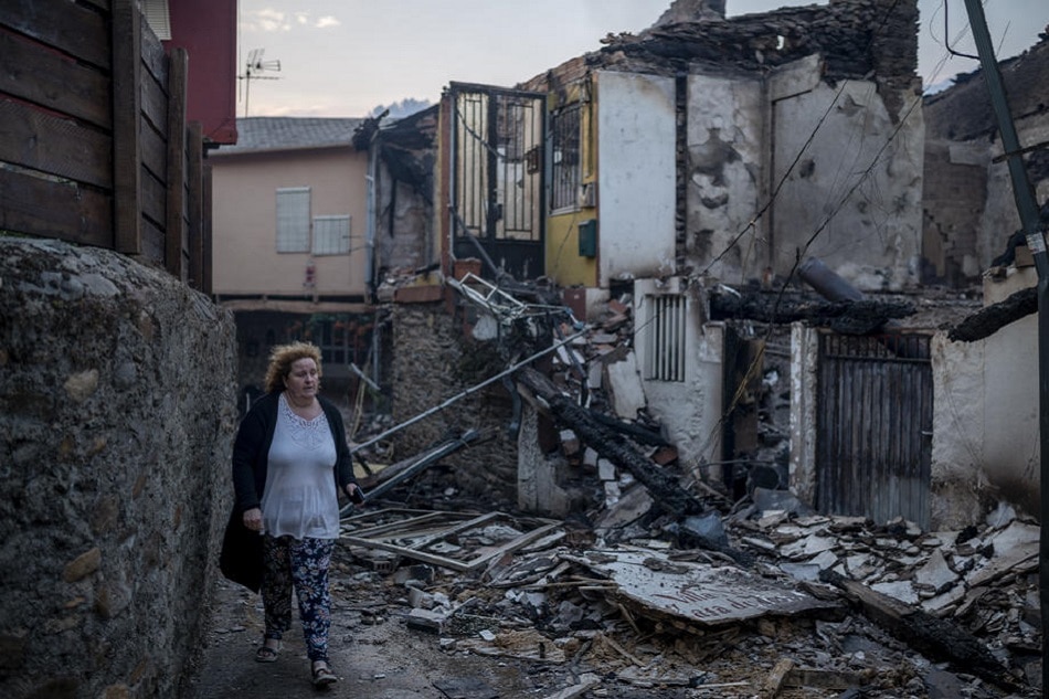 A woman passes by a burned house in Rubia, Spain, July 19, 2022. Wildfires recorded in Galicia have burnt over 18,835 hectares of forests in the region. Brais Lorenzo, EPA-EFE