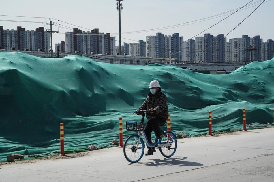 A migrant worker rides a bicycle near a construction site where is a new property plan in Beijing, March 21, 2022. Troubled Chinese property developer giant Evergrande and all its units suspended trading in Hong Kong on March 21, morning, according to a notice to the stock exchange. Wu Hong, EPA-EFE/file