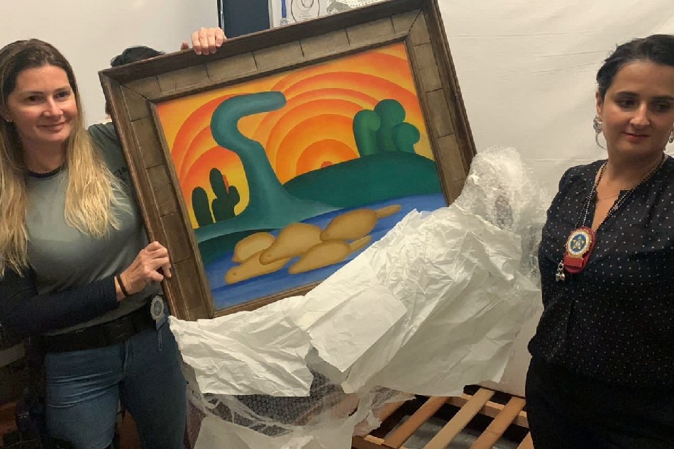 This handout picture released by Rio de Janeiro's Civil Police shows police officers holding the painting 'Sol Poente' by Brazilian artist Tarsila do Amaral in Rio de Janeiro, Brazil, on August 10, 2022. A woman was arrested Wednesday in Brazil for allegedly stealing artworks, jewelry, and money worth some 725 million reais (USD 145 million) from her mother in a heist that went on for months, police told AFP. Among the 16 paintings stolen were 'O Sono' and 'Sol Poente' by Brazilian artist Tarsila do Amaral, estimated at several tens of millions of dollars each, according to local press. RIO DE JANEIRO CIVIL POLICE / AFP