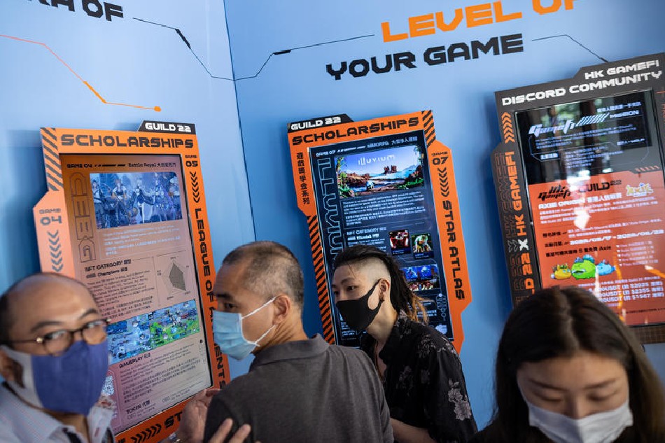 A man (2-R) introduces play-to-earn blockchain games to visitors in a pop-up shop promoting blockchain in Hong Kong, China, 17 May 2022. Blockchain games are different from traditional games in that they offer economic incentives, NFT, (Non-Fungable Tokens), and rewards exchangeable for crypto-currency by progressing through the different games levels. EPA-EFE/JEROME FAVRE/FILE