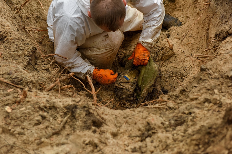 A forensic technician inspects a body in a grave near Izyum, Kharkiv region, northeastern Ukraine, 16 September 2022. A mass burial site was found after Ukrainian troops recaptured the town of Izyum. According to the head of the investigative department of the police of the Kharkiv region, the burial site, one of the largest in a recaptured city so far, counts more than 440 separate graves. The Ukrainian army pushed Russian troops from occupied territory in the northeast of the country in a counterattack. Kharkiv and surrounding areas have been the target of heavy shelling since February 2022, when Russian troops entered Ukraine starting a conflict that has provoked destruction and a humanitarian crisis. EPA-EFE/OLEG PETRASYUK -- ATTENTION EDITORS: GRAPHIC CONTENT
