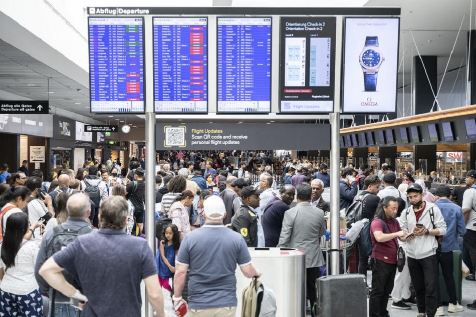 Passengers wait in front of a display board at Zurich airport, Switzerland, June 15, 2022. Ennio Leanza, EPA-EFE/file